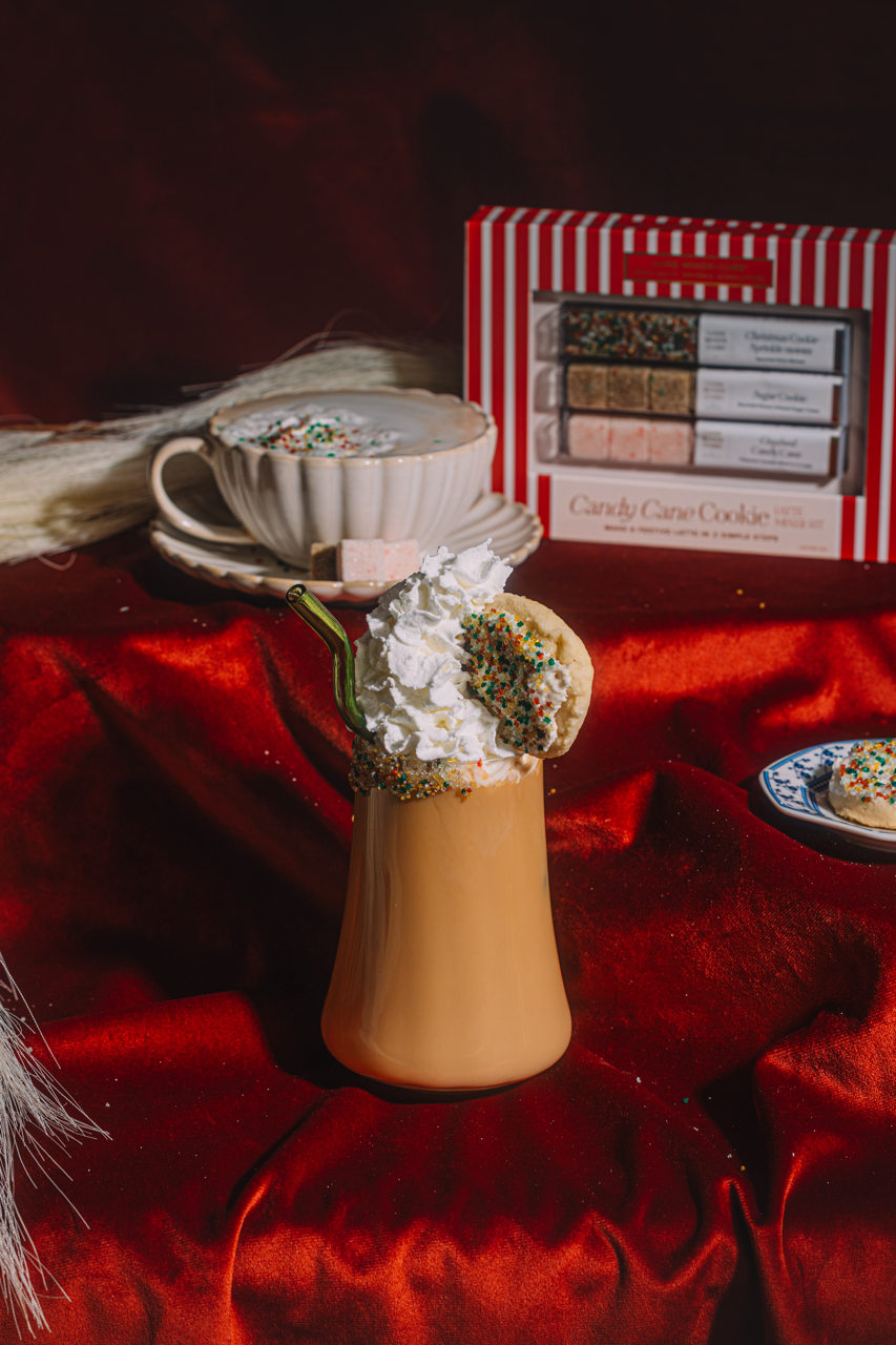 Latte with whipped cream, sprinkles, and striped cookie bar set box behind