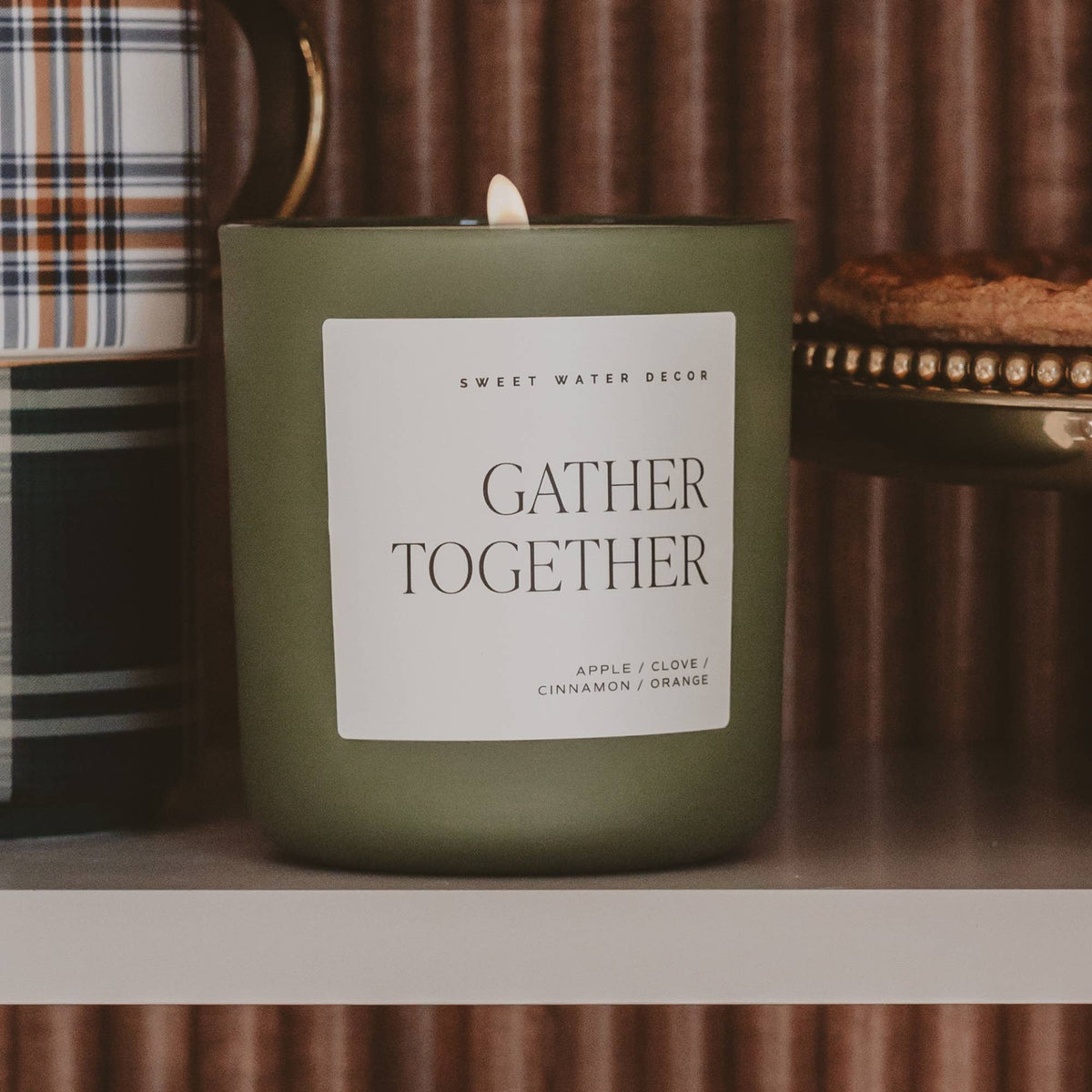 Olive green soy candle jar with lit wick and white label reading Gather Together