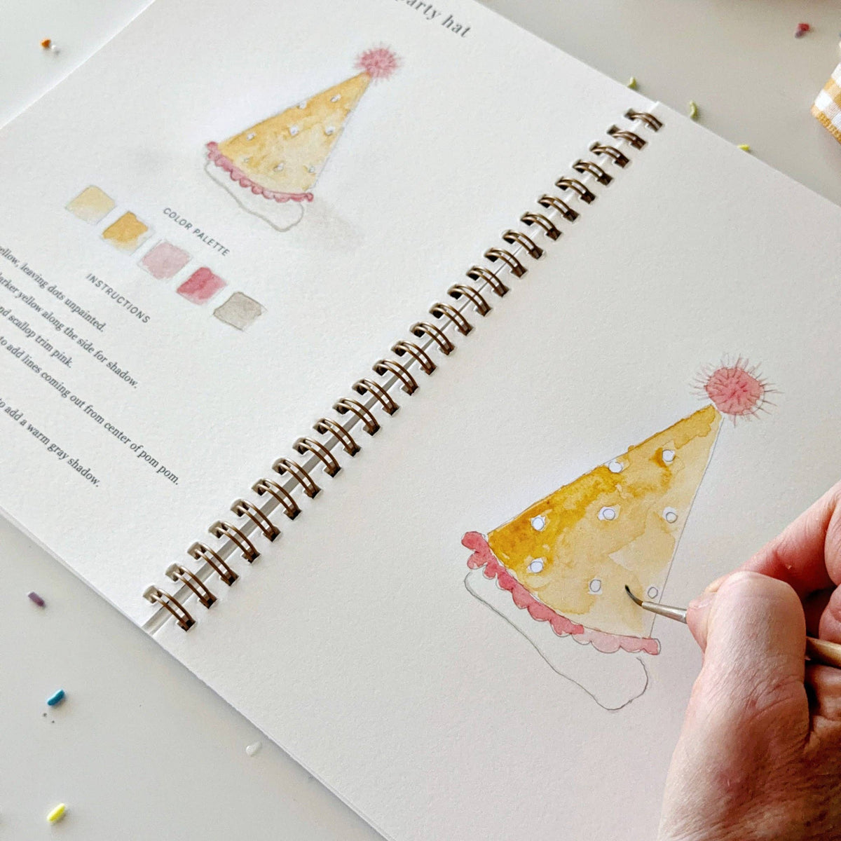Watercolor workbook sketch page with cake drawing and spiral binding, hand coloring.