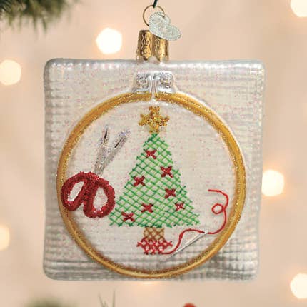 Round cross-stitch Christmas ornament with green tree and red accents, gold hanger loop