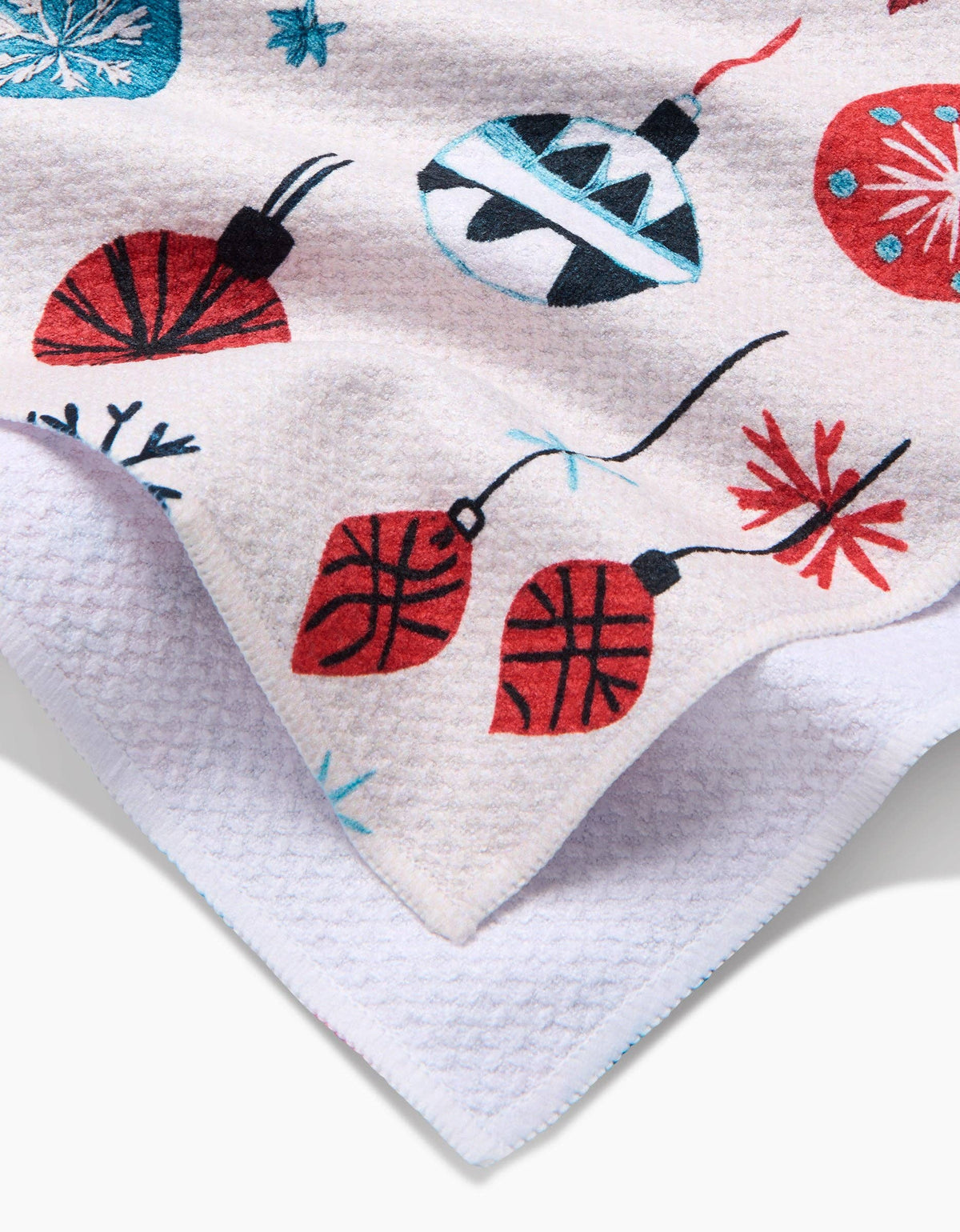 Corner of white tea towel with embroidered red and blue ornament motifs