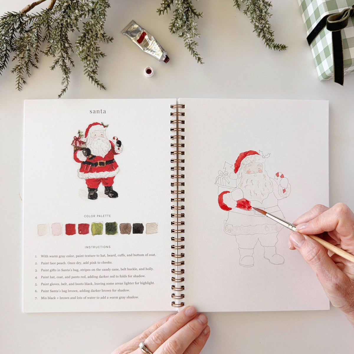 Christmas watercolor workbook open spread with Santa palette page and brush painting a figure