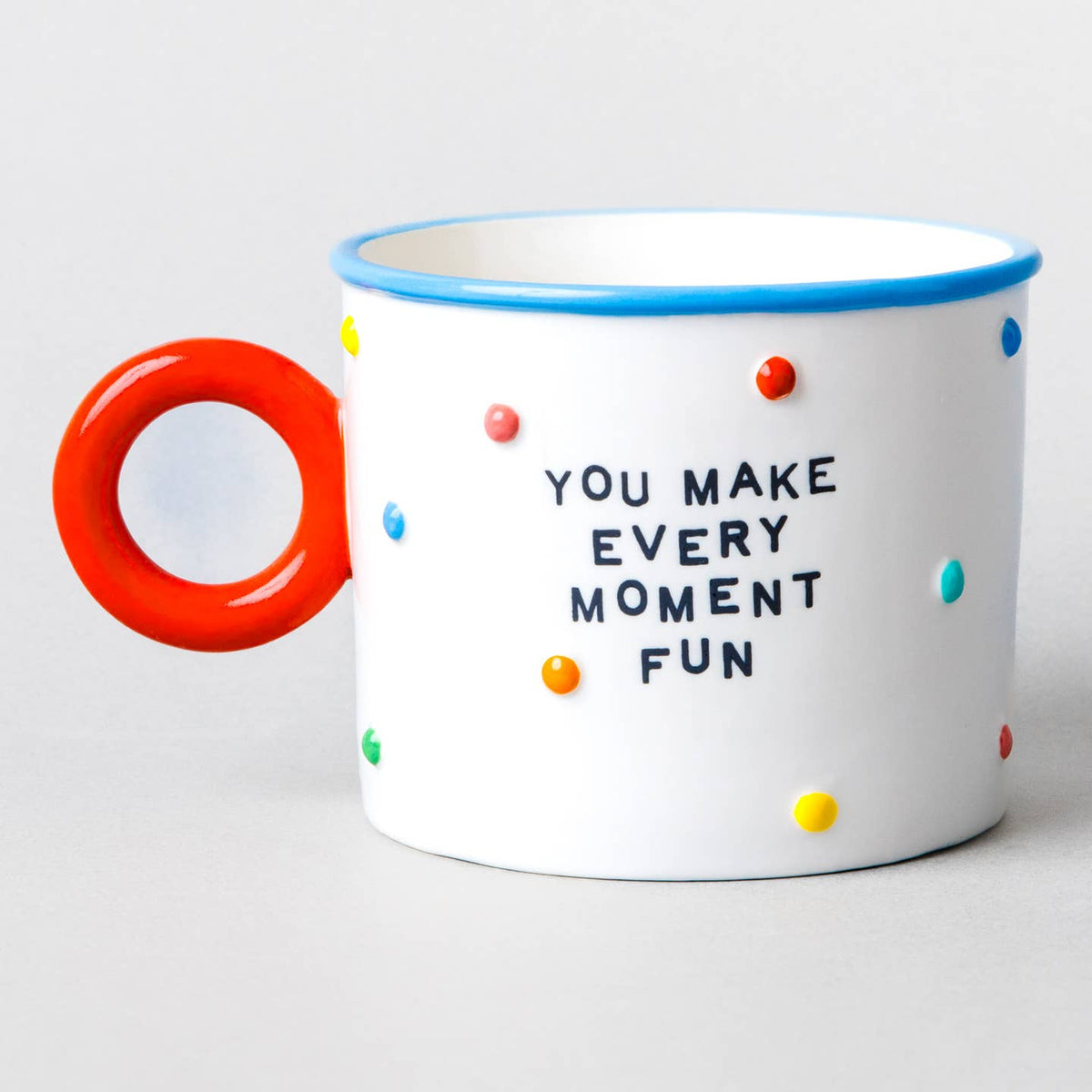 White ceramic mug with red handle, blue rim, colorful dots, “You Make Every Moment Fun”