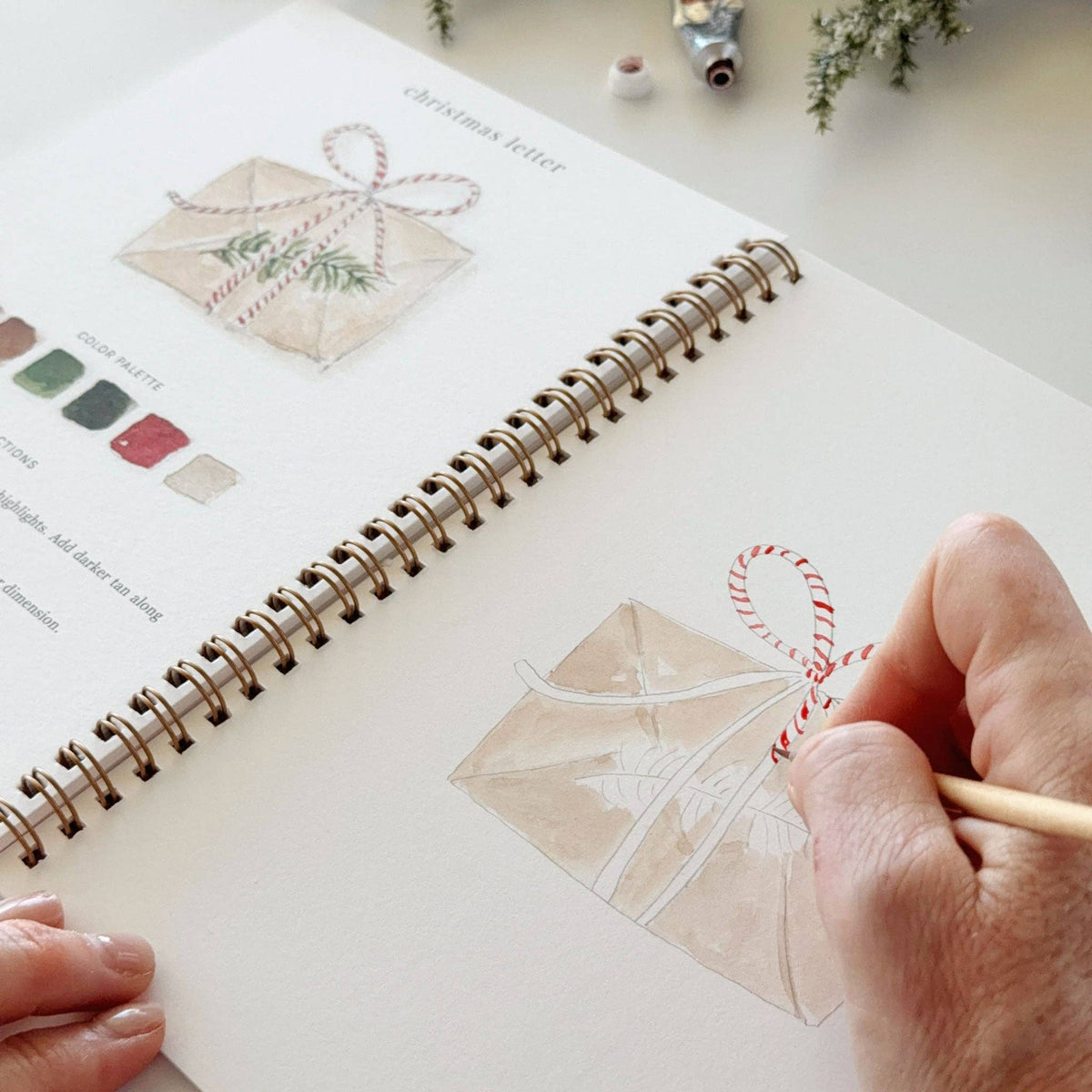 Christmas watercolor workbook close page with envelope outline and hand using a paint brush