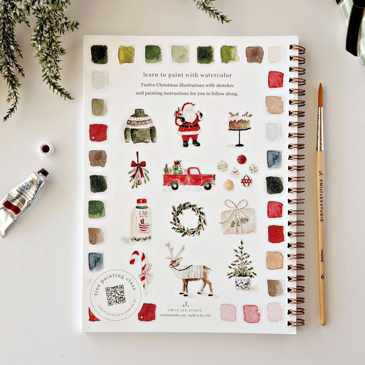 Christmas watercolor workbook open page with watercolor palette border and holiday illustrations