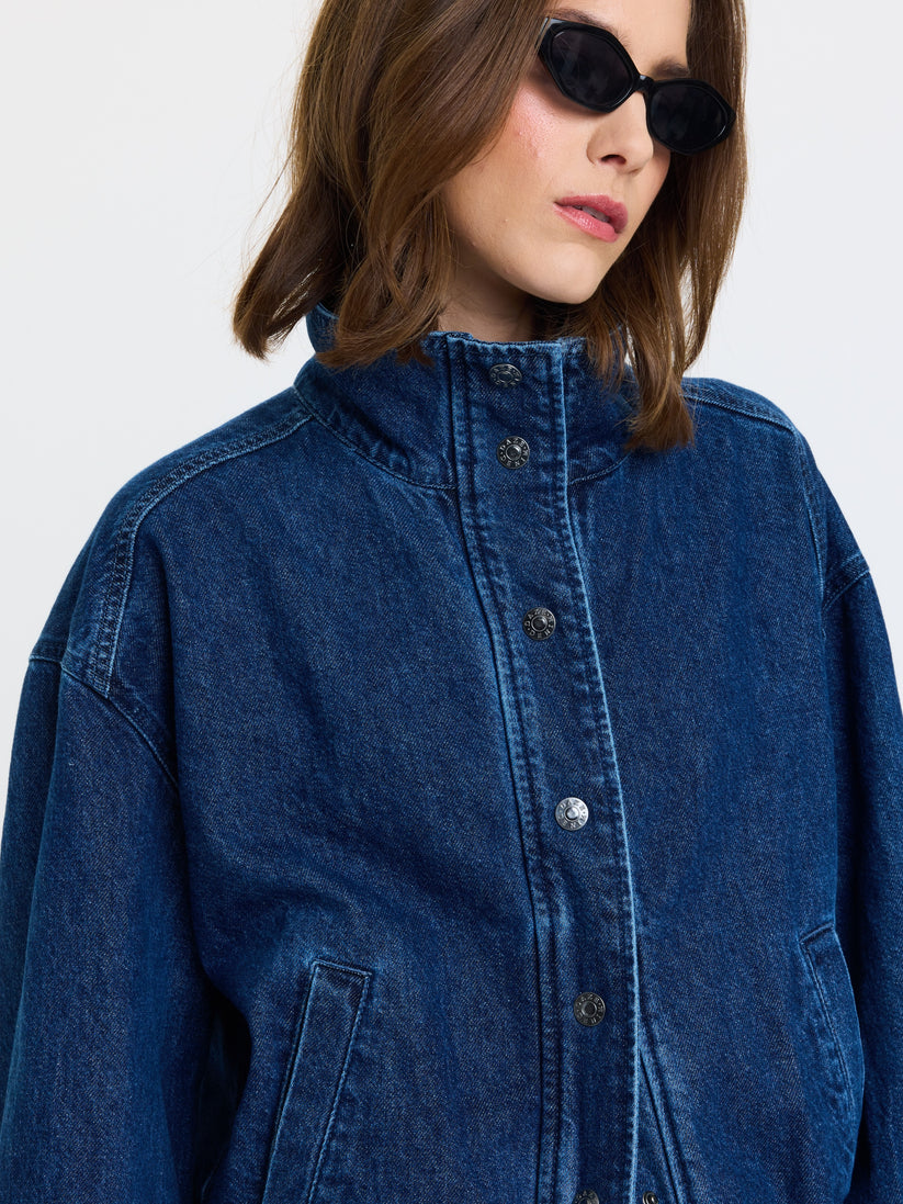 Blue denim funnel-neck jacket close-up: button placket and stitched seam details