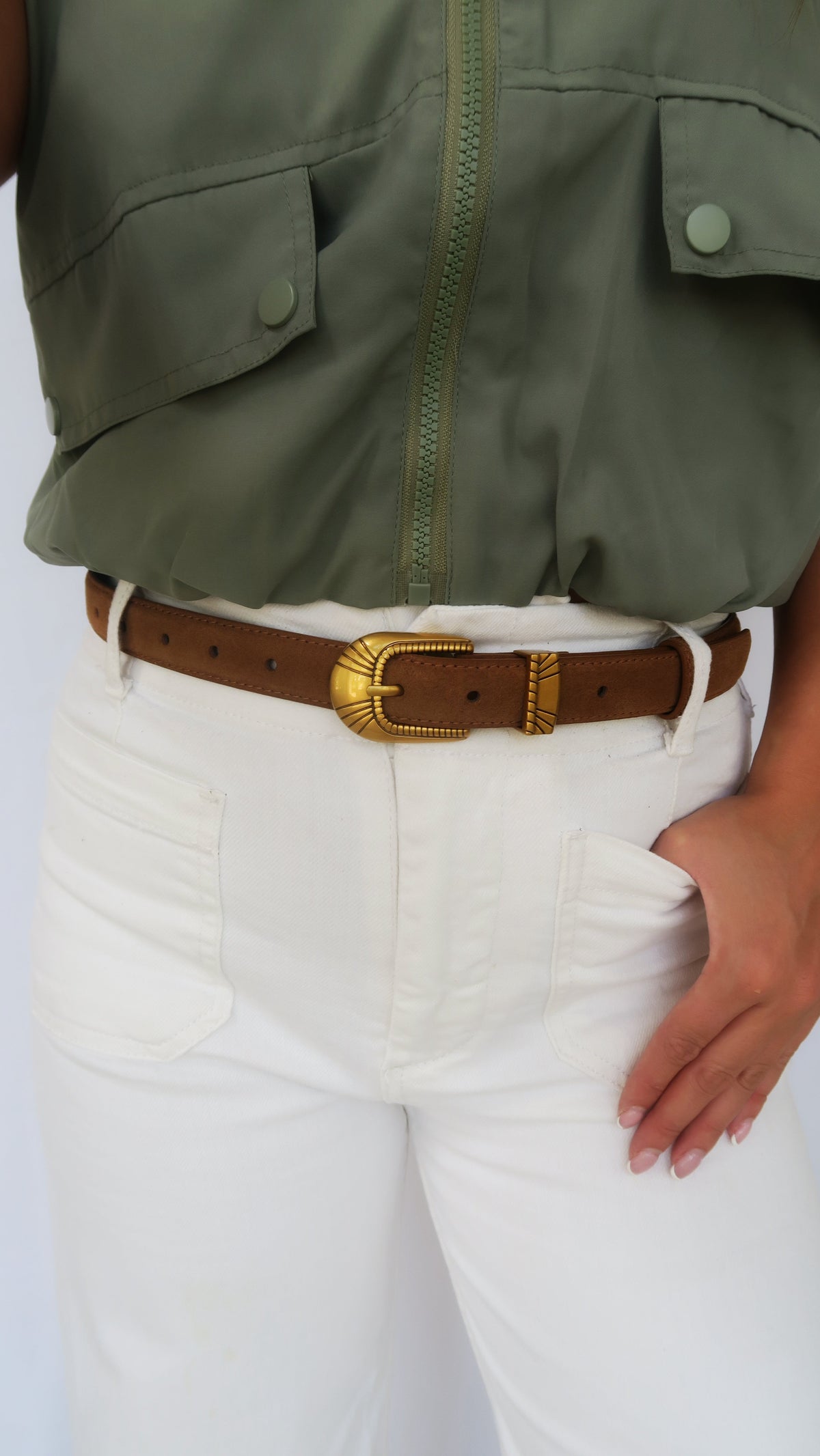 Brown belt with gold-tone oval buckle worn at waist over white jeans