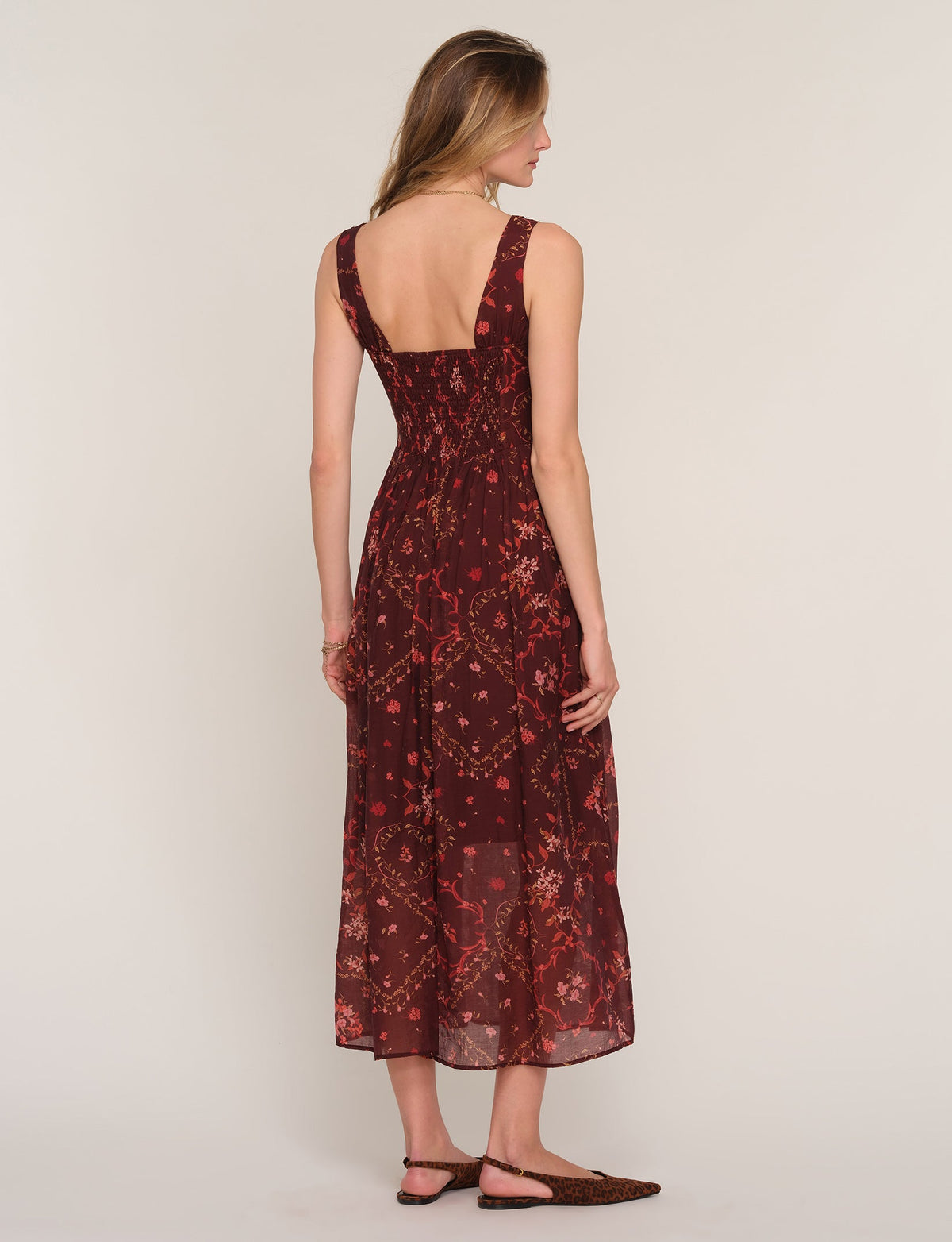 Back view of sleeveless midi dress in dark burgundy floral print with draped skirt