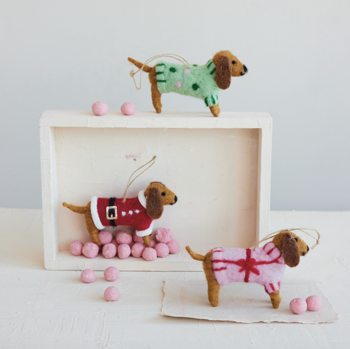 Felt dachshund ornaments in sweaters (green, red, pink) with hanging twine on display