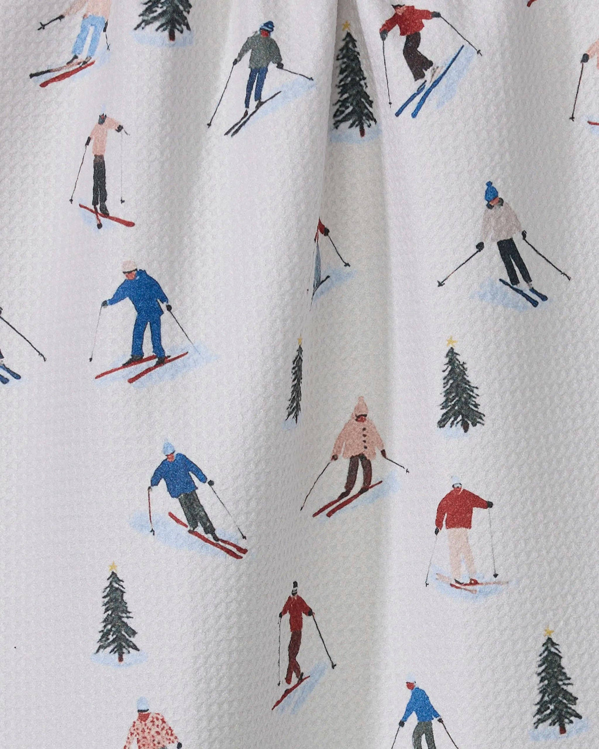 Printed tea towel fabric close-up with skiers, pine trees, and white background
