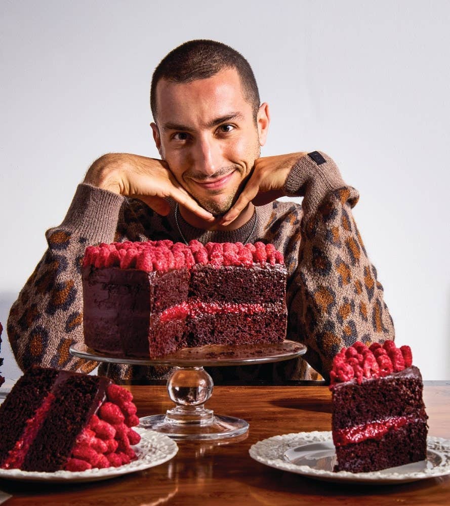 Man in a leopard print sweater holding a frosted cake on a platter.