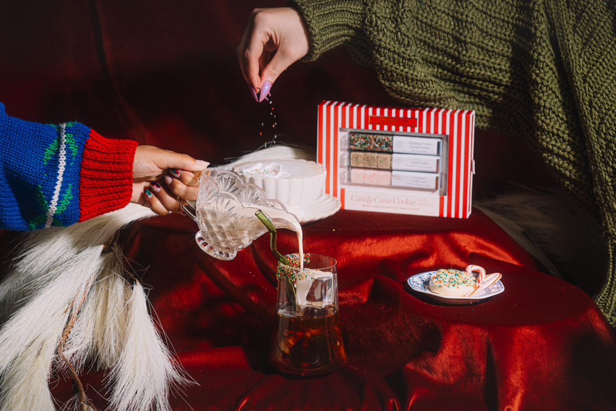 Two people setting a cookie latte with glass carafe, whipped cream cup, and gift box
