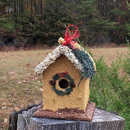 Yellow birdhouse decoration with wreath window and red bow on outdoor stand