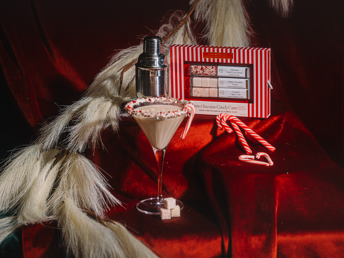 Martini glass with candy cane garnish beside striped martini kit box and shaker