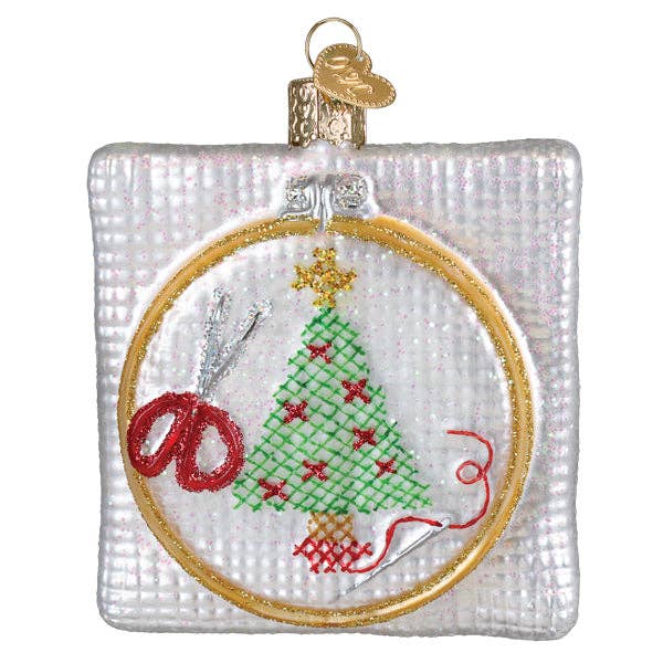 Framed round cross-stitch Christmas ornament with green tree and red accents, gold hanger