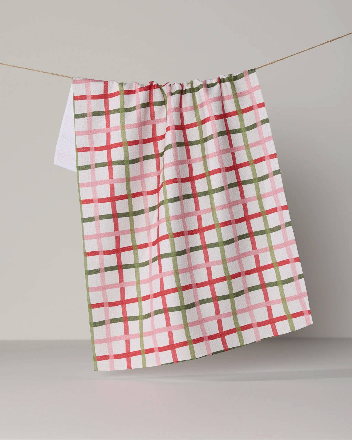 Plaid tea towel, red and green grid on white, hanging with gathered top hem