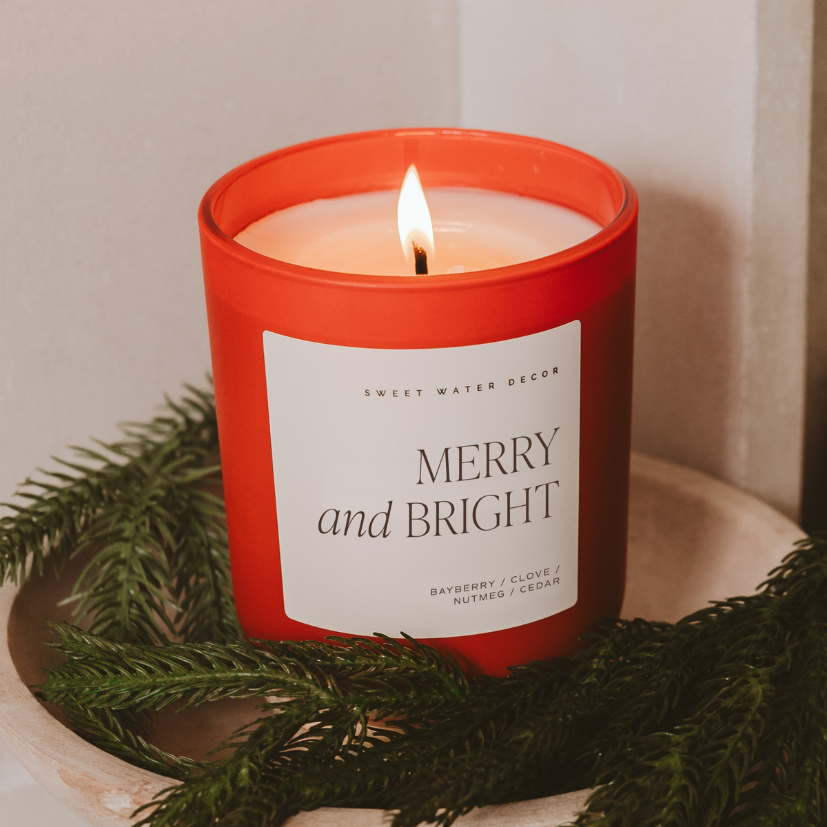 Red soy candle with “MERRY and BRIGHT” label and burning flame