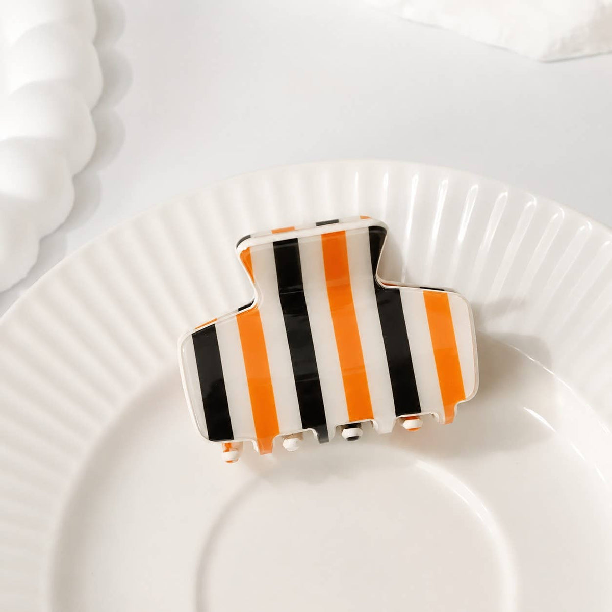 Striped hair claw clip with white, orange, and black vertical stripes