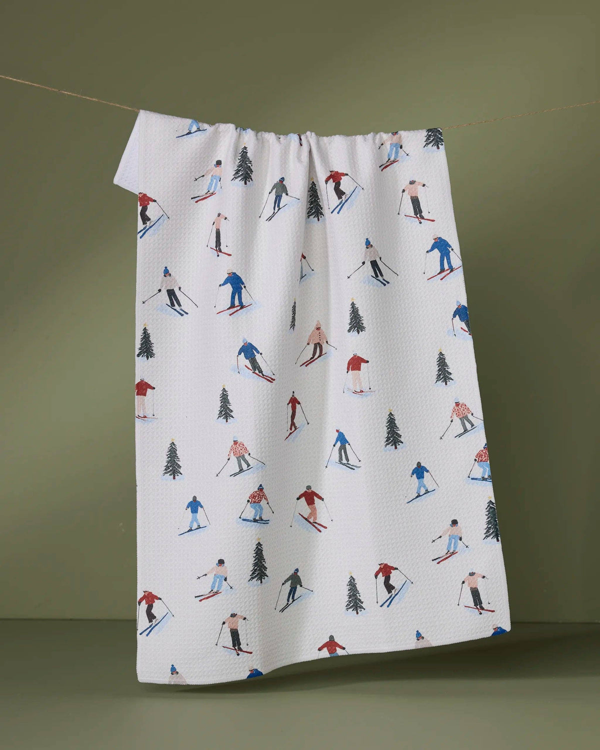 Printed tea towel with winter skiing figures and pine trees on white, gathered top hem