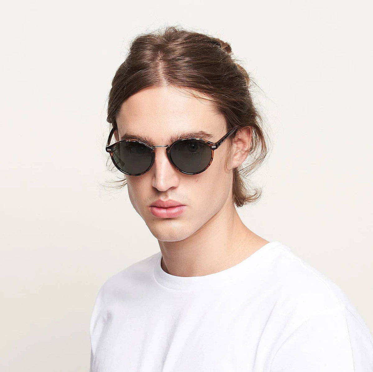 Round black sunglasses with dark lenses worn on model’s face