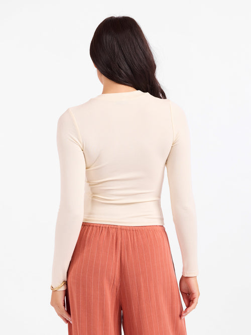 Back view of cream fitted crewneck long-sleeve top with smooth seams and hem