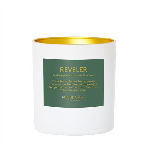 Reveler candle in white jar with gold rim, green label on the front