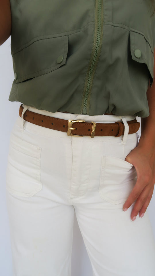 Brown leather belt with gold-tone rectangular buckle worn on white jeans, close-up.