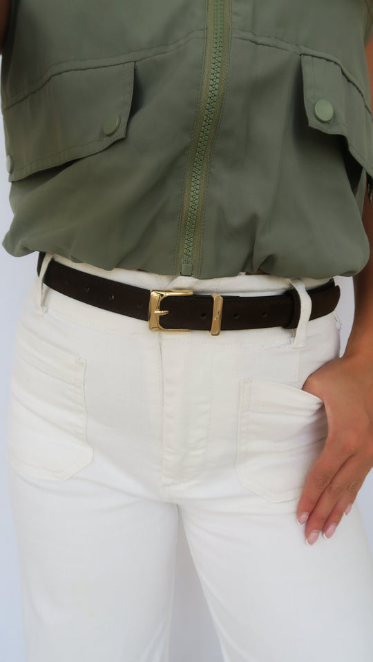 Brown leather belt with gold-tone rectangular buckle worn on white pants, side view.