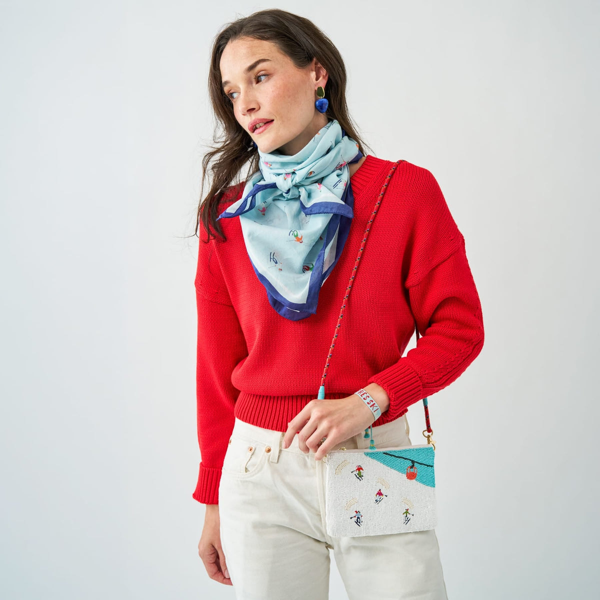 White embroidered clutch with ski figures and turquoise trim, held across red sweater outfit