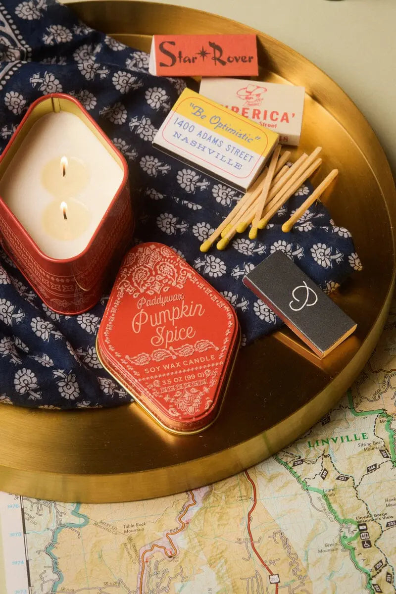 Red decorative candle tin with 'Pumpkin Spice' label and visible wick
