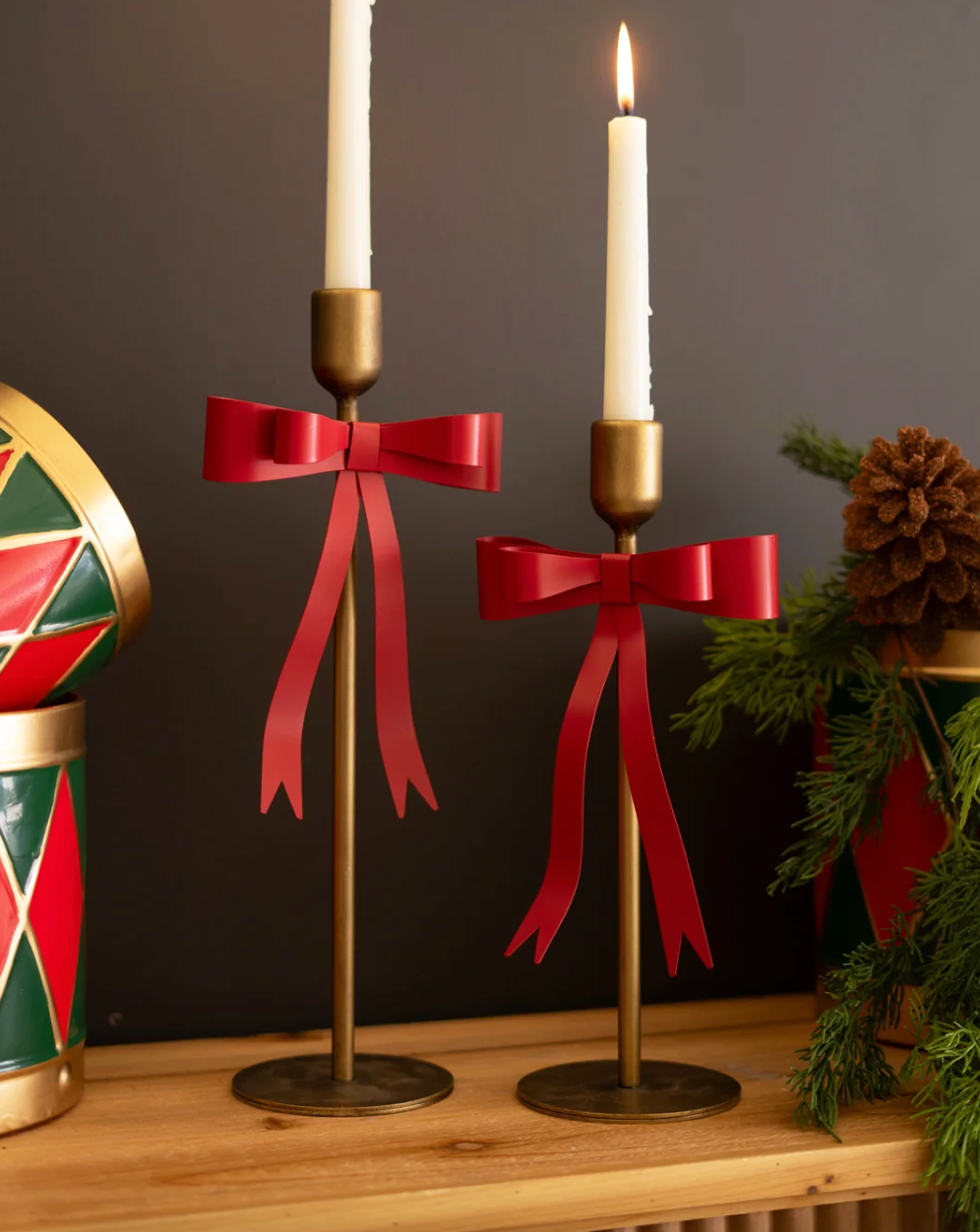Red ribbon bow taper candle holders with gold-tone bases, holding lit taper candles