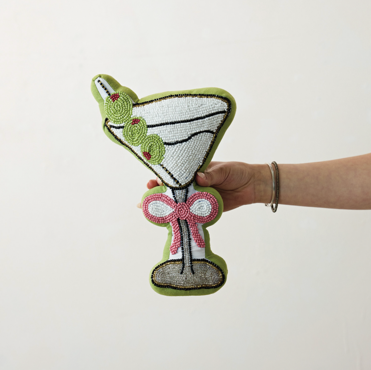 Martini-shaped beaded pillow held in hand; white glass, red bow, green olives