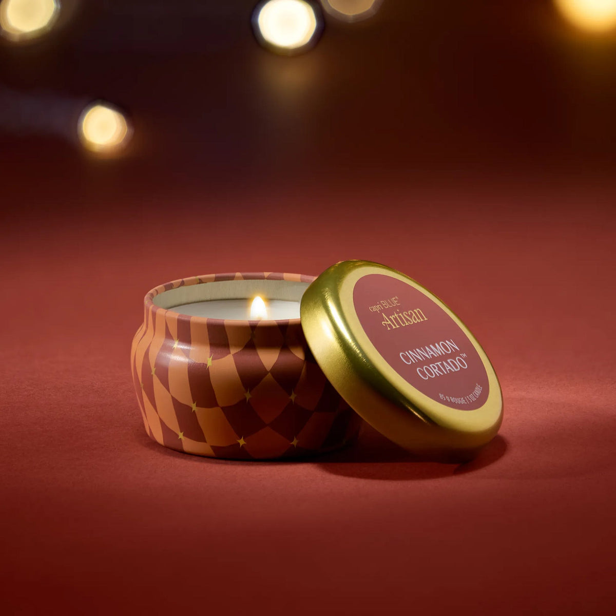 Mini candle tin with patterned sides and gold lid, lit wick inside