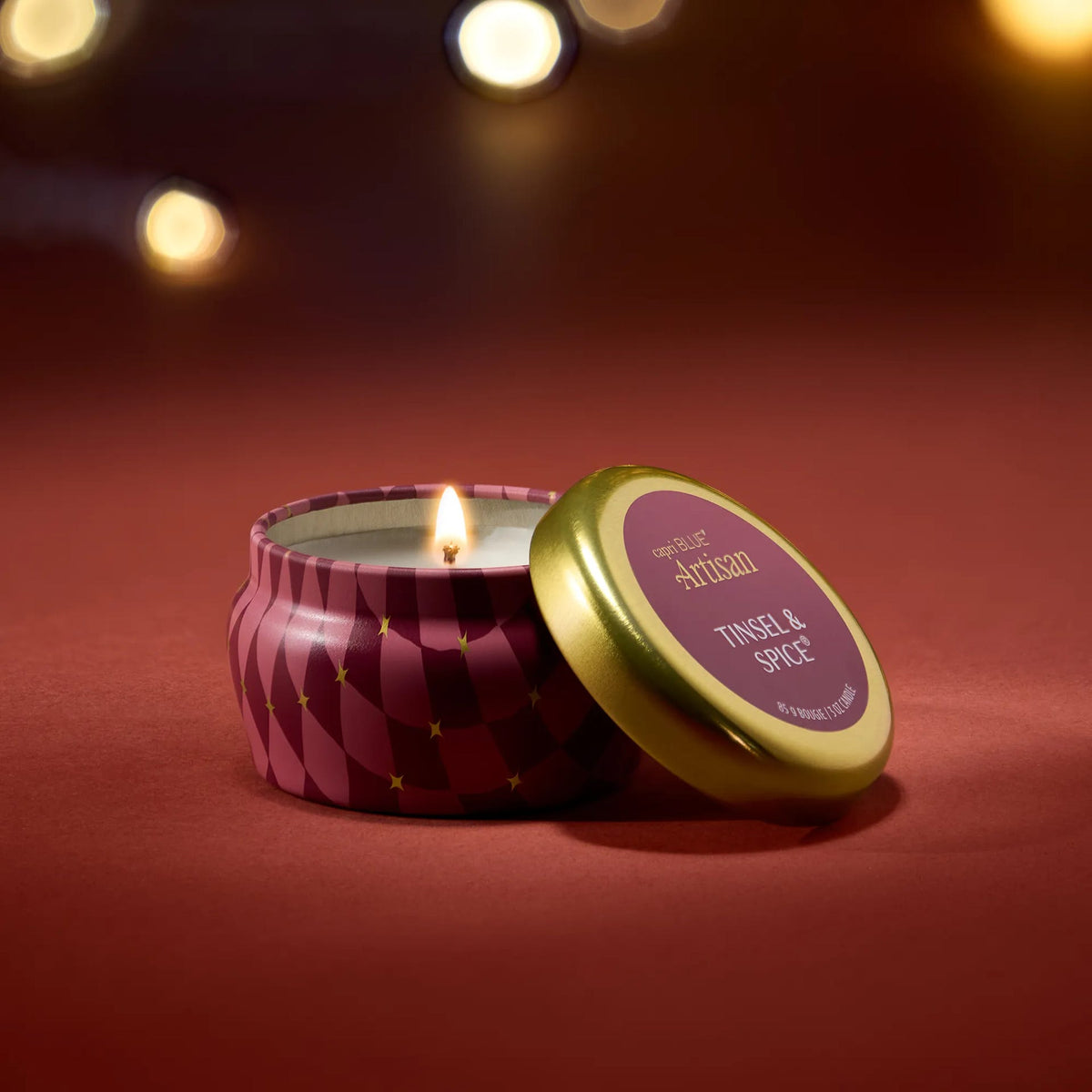Mini scented candle in maroon diamond-patterned tin with gold lid, lit wick