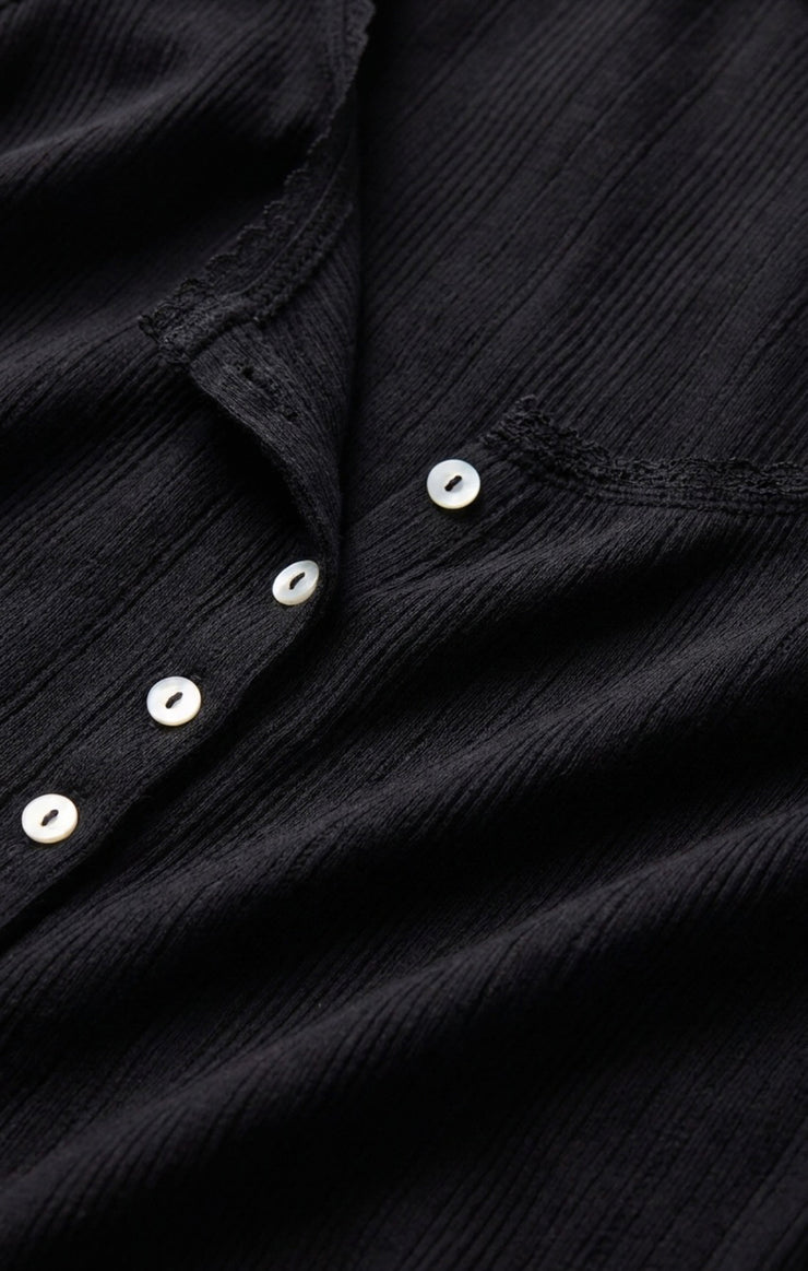 Black pointelle knit fabric with white round buttons along the front placket.