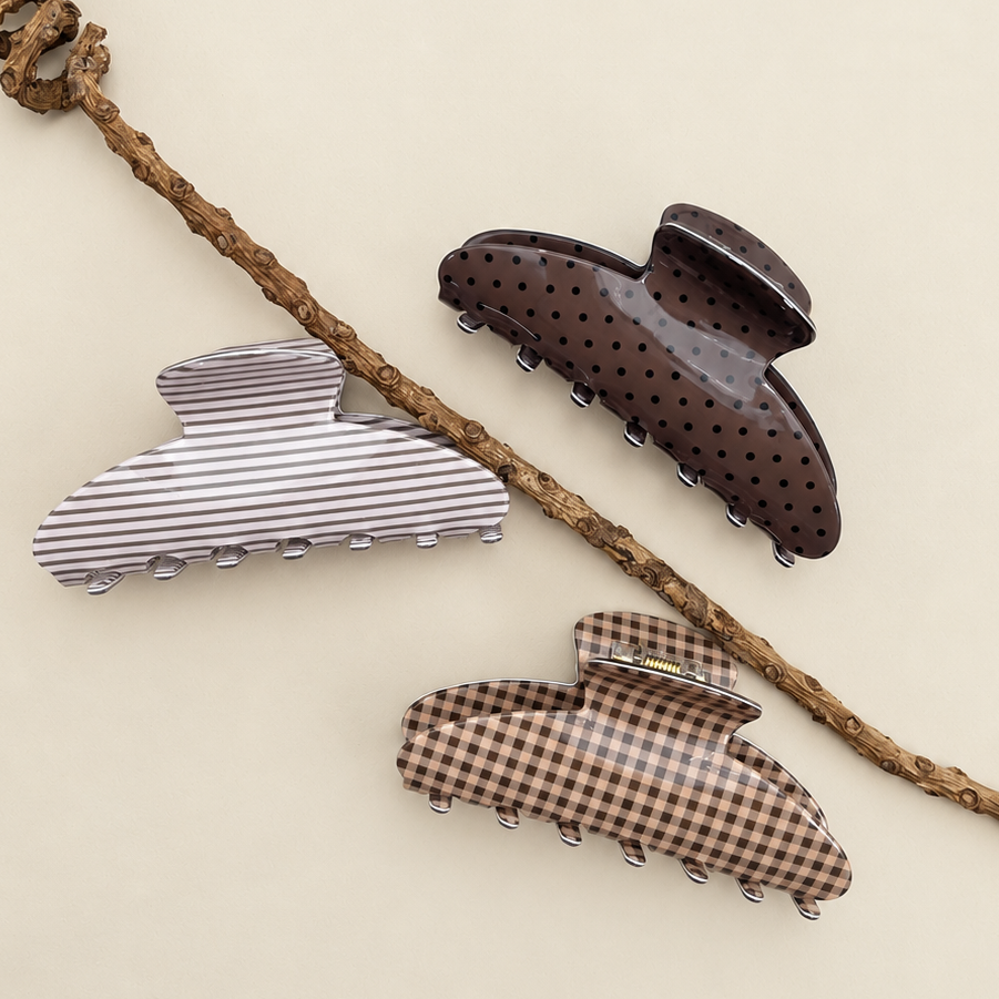 Oval jumbo hair claw clips in brown plaid, gray stripe, and dark polka-dot patterns.