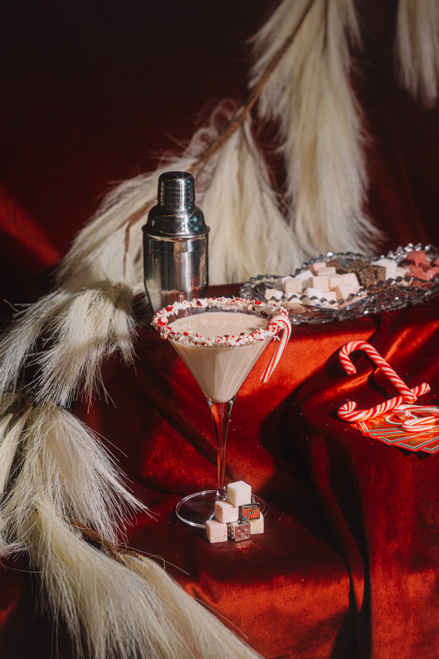 Martini glass with candy cane garnish, next to a cocktail shaker and wrapped mix