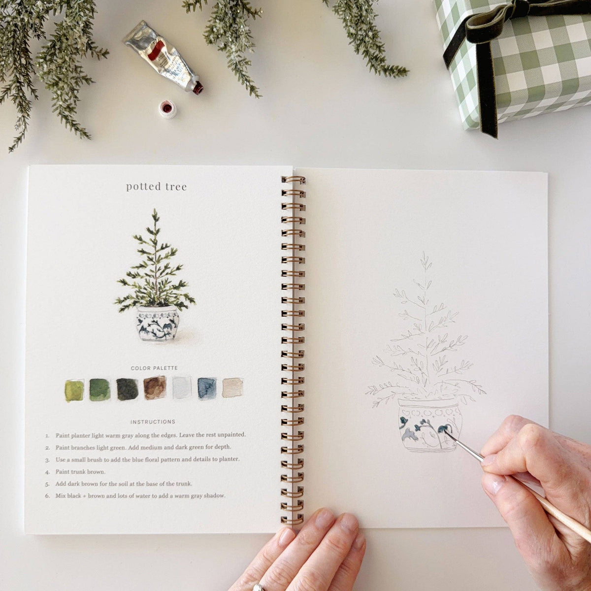 Christmas watercolor workbook open spread with potted tree guide and brush painting a sketch