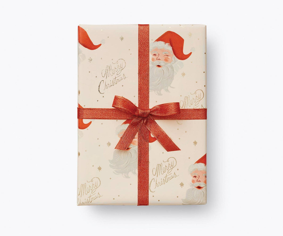Santa-themed gift wrap paper with red ribbon bow and repeating Santa face pattern