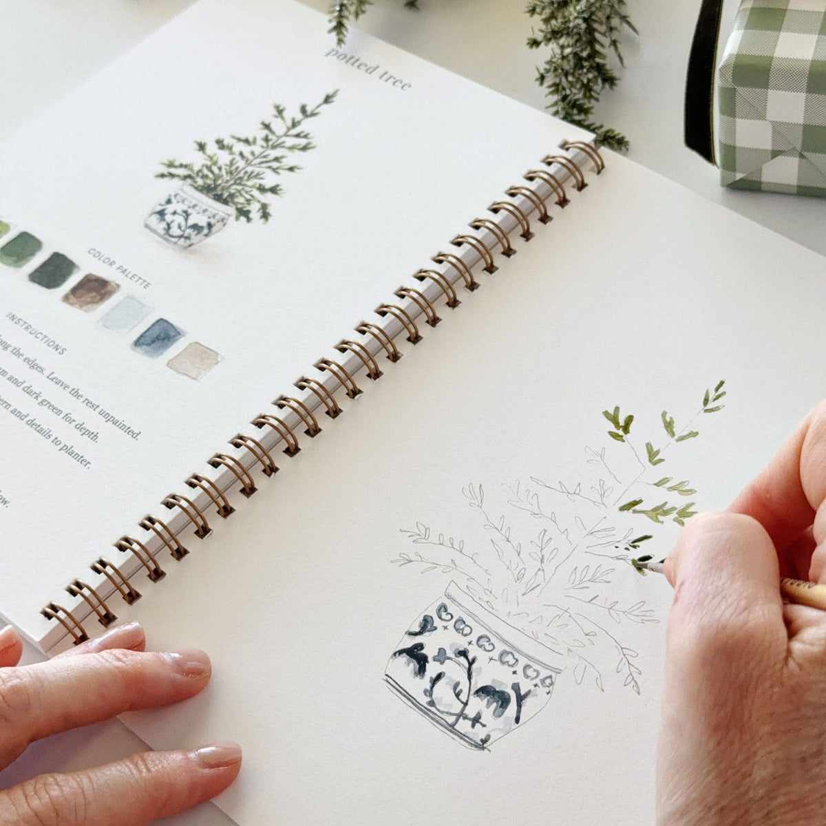 Christmas watercolor workbook close page with potted tree sketch and hand painting greenery