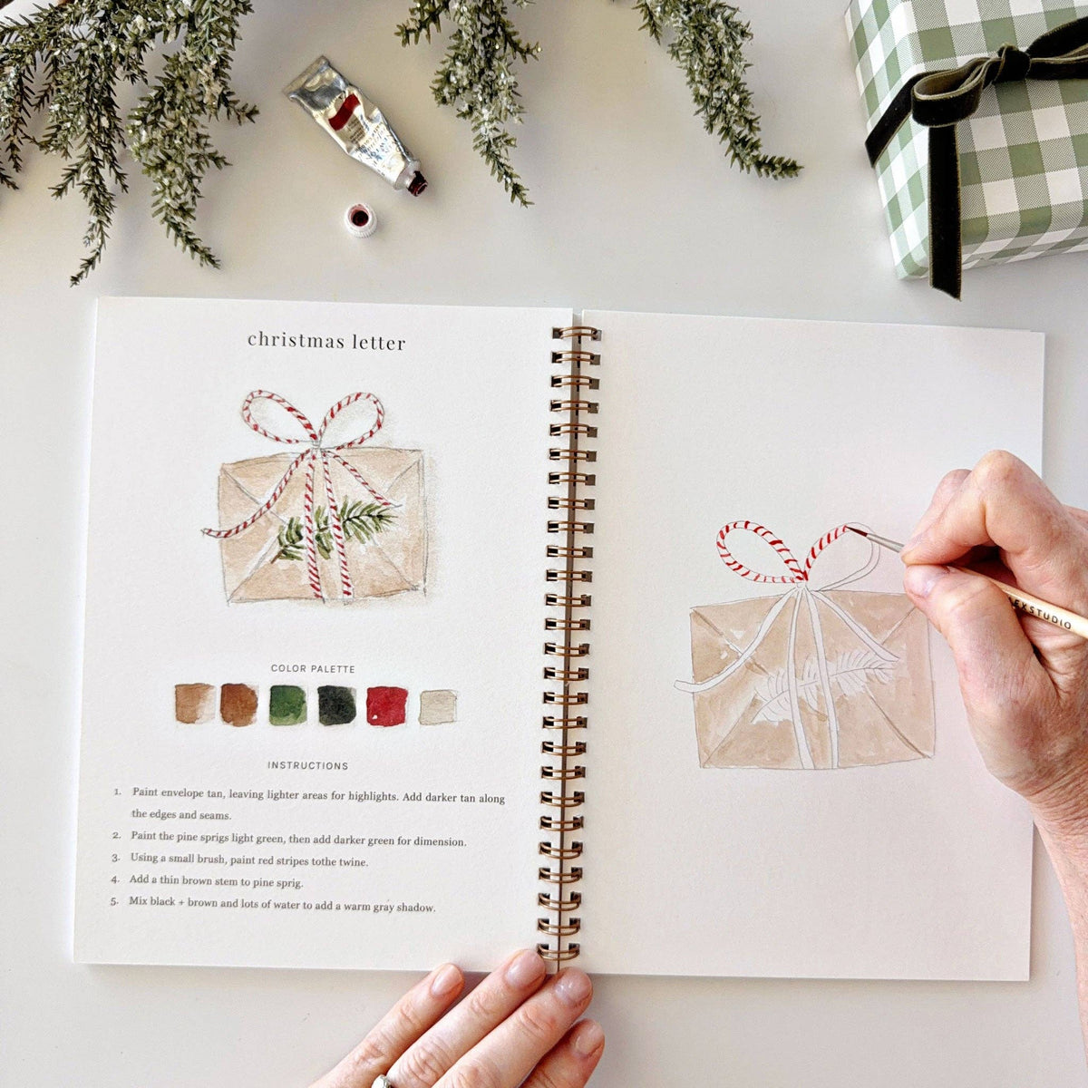 Christmas watercolor workbook open page with gift-envelope illustration and hand painting details