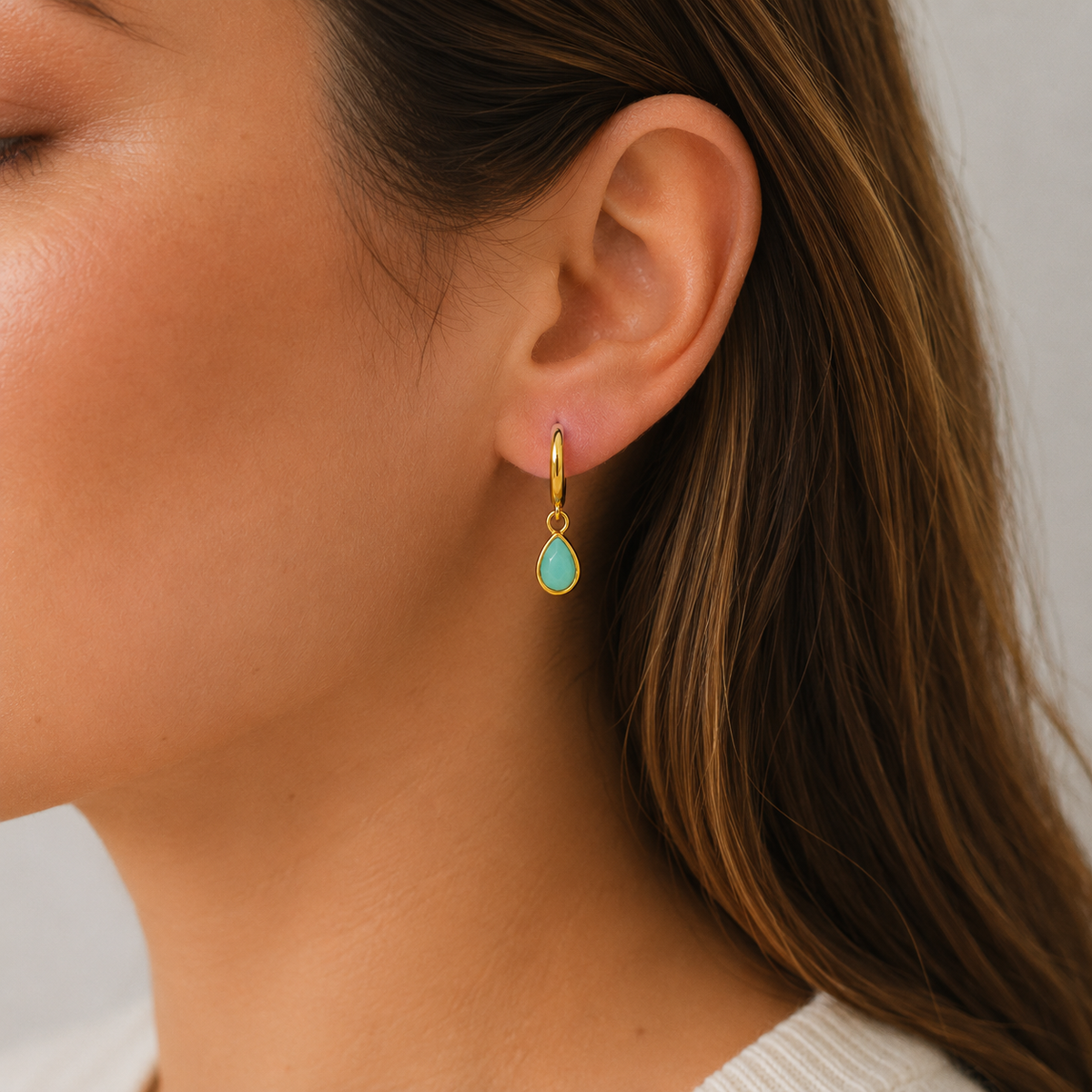 Gold hoop earrings with dangling light-blue teardrop charms, close-up on ear