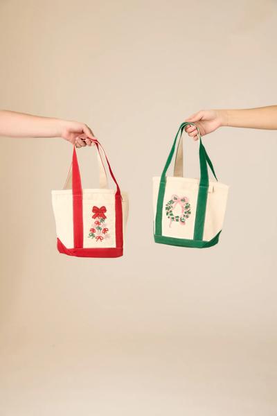 Two mini tote bags held up, red and green, each with embroidered holiday patch